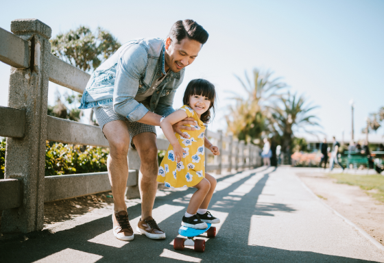 Smiling man holding a small happy child on a skateboard