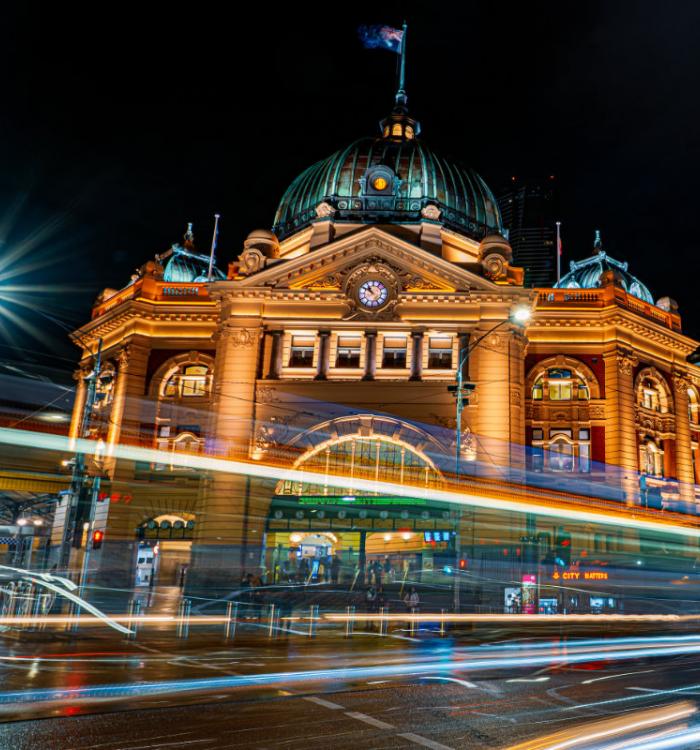 A photo of Flinders Street Station in Melbourne at night with time-lapse photography to make the car lights streak across the photo